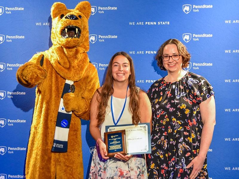 Nittany Lion with female student and female faculty member displaying an award.
