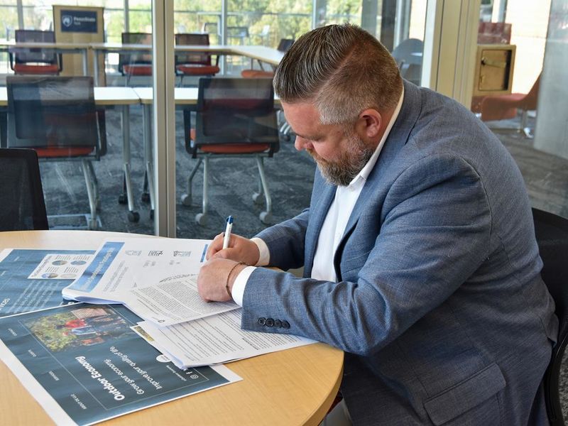 Man in a suit at a table writing on documents.