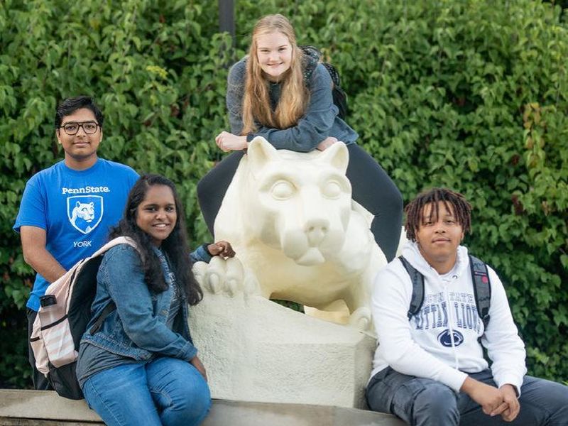 Two female and two male students sitting on and around the Nittany Lion Shrine