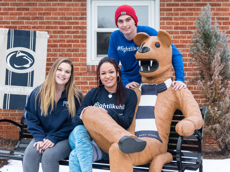 Students sit with the Nittany Lion statue on a bench in winter