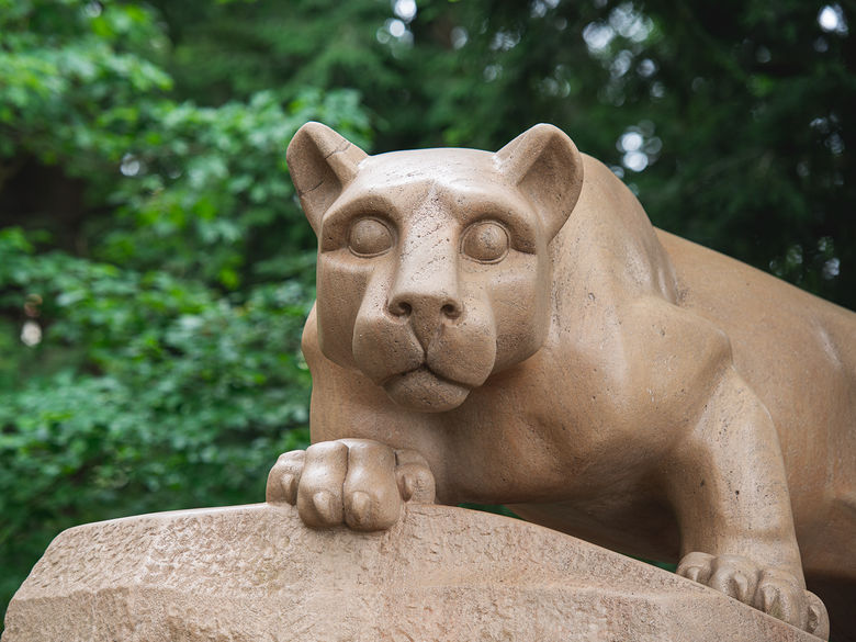 Penn State Nittany Lion Shrine in the summer, surrounded by green foliage.