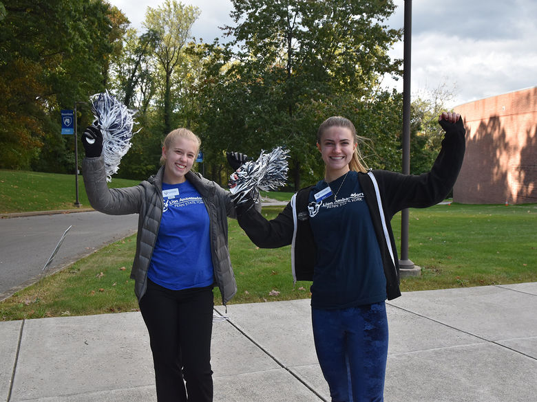 Two female students shaking pom-poms and smiling