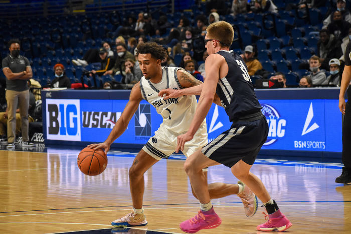 Two basketball players on the court, one dribbling the ball and the other trying to stop him