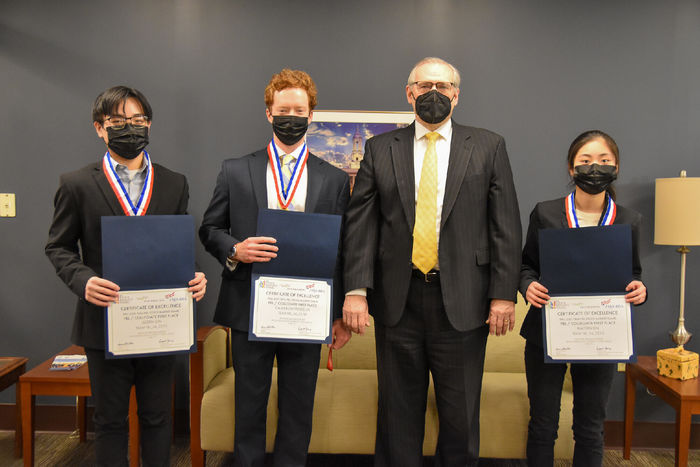 Four people, three students, and one adult, pose for a photo with certifcates for a first-place win in a national competition 