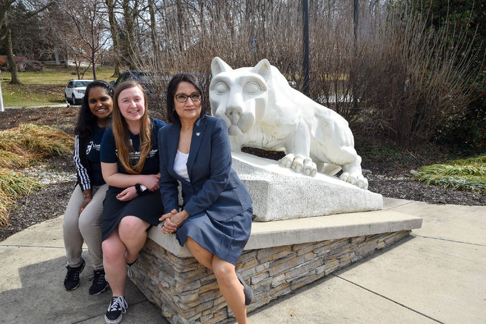 Two female students and an older female sit together by the Nittany Lion Shrine at Penn Stae York. 
