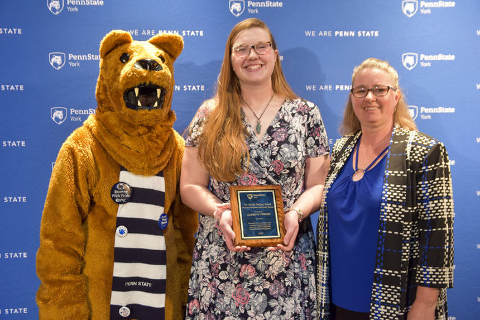 Person dressed in Nittany Lion costume and two femailes with glasses are opart of an award presentation.