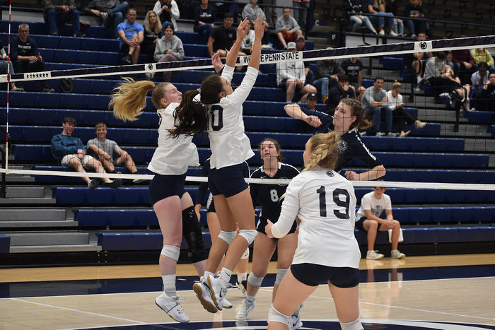 Four women's volleyball players at the net with two going up for a hot and the other defending