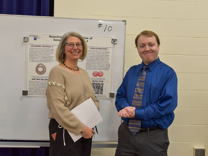 Female faculty member, wearing glasses, and male stuent at display board