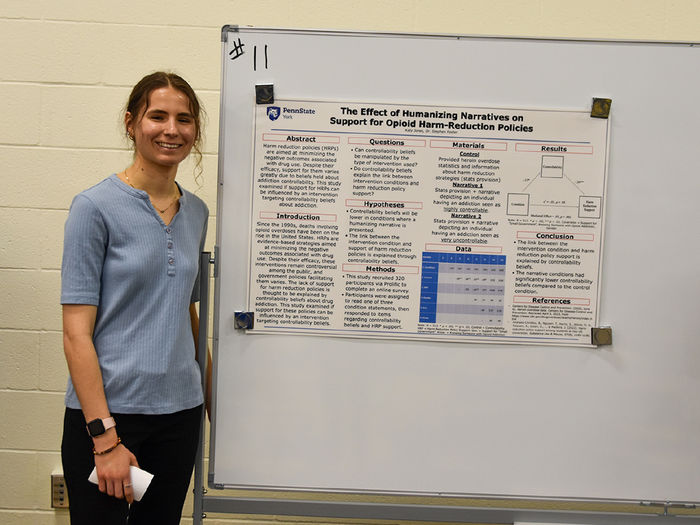 Young woman with hair in a ponytail stands in front of her research poster