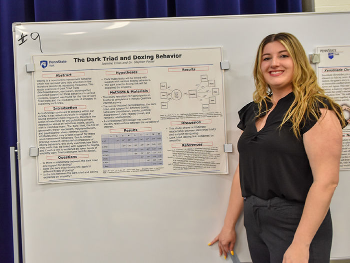 Female student with long blonde hair standing in front of her research poster
