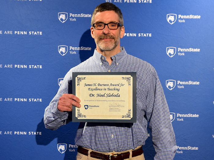 Male faculty member wearing glasses and holding a certificate.