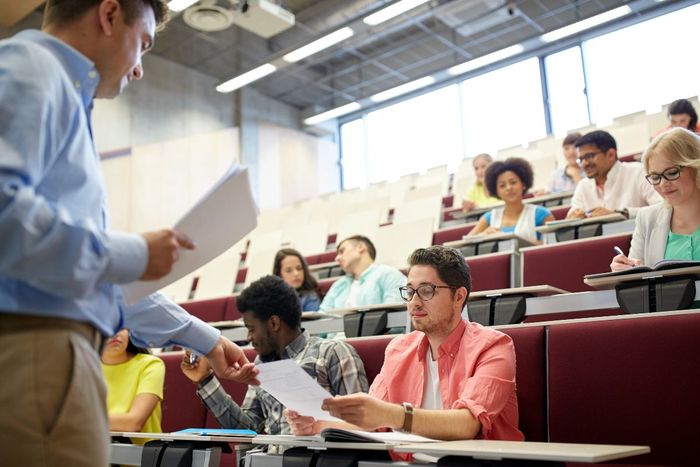 Professor hands papers to students in a lecture hall.