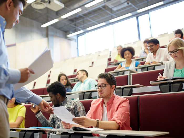 Professor hands papers to students in a lecture hall.