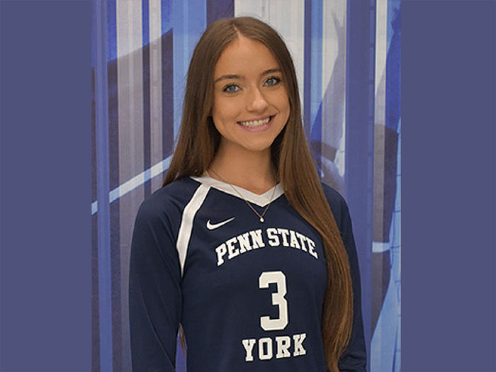 Young female with long brown hair wearing a blue and white Penn State York volleyball jersey.