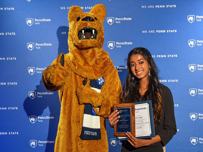 Nittany Lion character with female student of color holding an award.