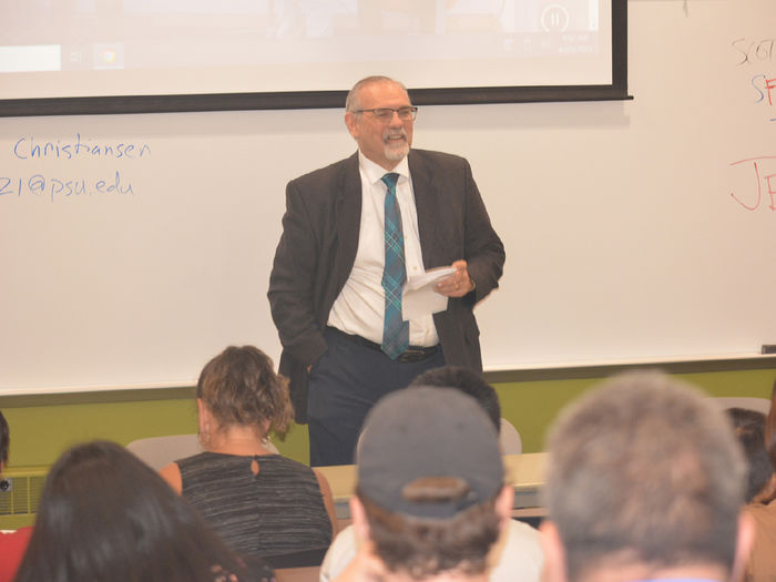 Older adult Caucasian male wearing a suit and glasses talking to a group