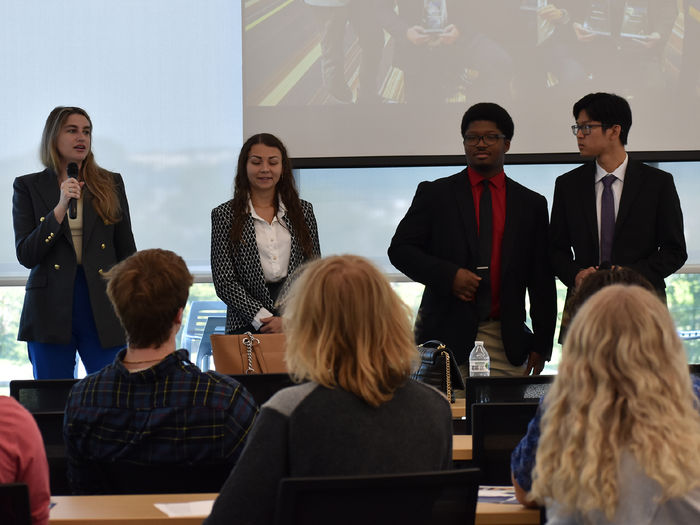 Two females and two males dressed in business attire in front of a group