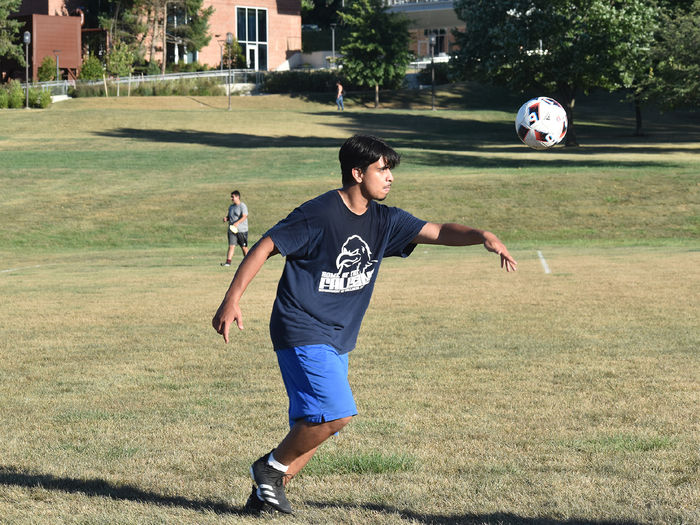 Male soccer player runs with a soccer ball in the air.