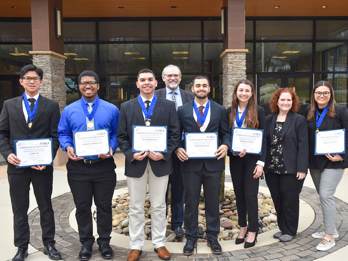 Eight males and females pose with awards in front of building.