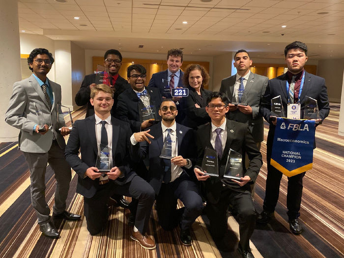 A group of nine students, holding awards, stands with their faculty member and adviser