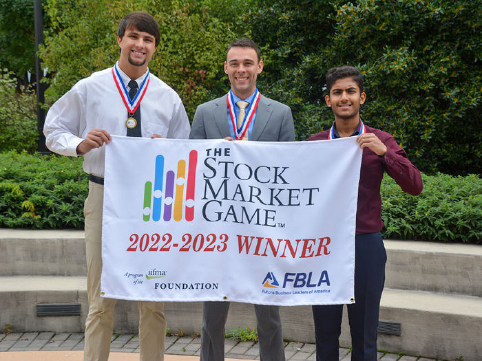 Three male students holding banner.