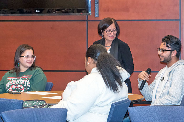 A student speaks into the microphone as a professor and other students listen.