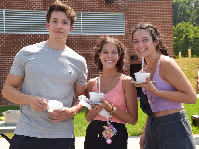 Young male and two females enjoying ice cream outside.