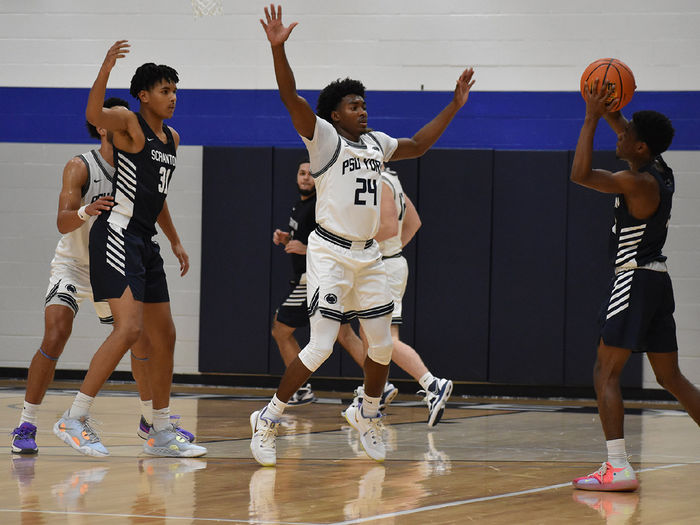 Basketball players on the court with one African American playing raising his arms to block a pass