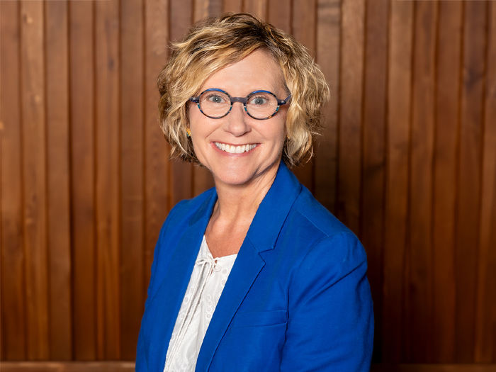 Headshot of adult female with blonde hair and wearing glasses, dress in a suit