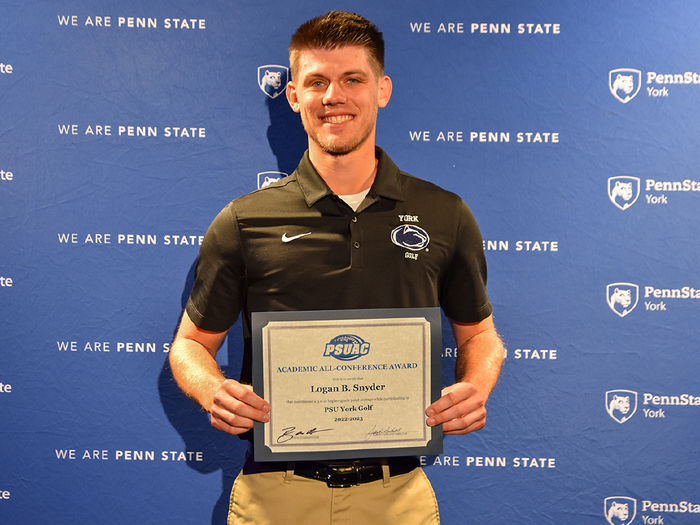 Male student-athlete holding an award certificate standing in front of a banner