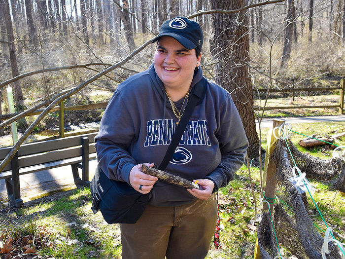 STudent wearing a Penn State hat and sweat holds a lichen sample/