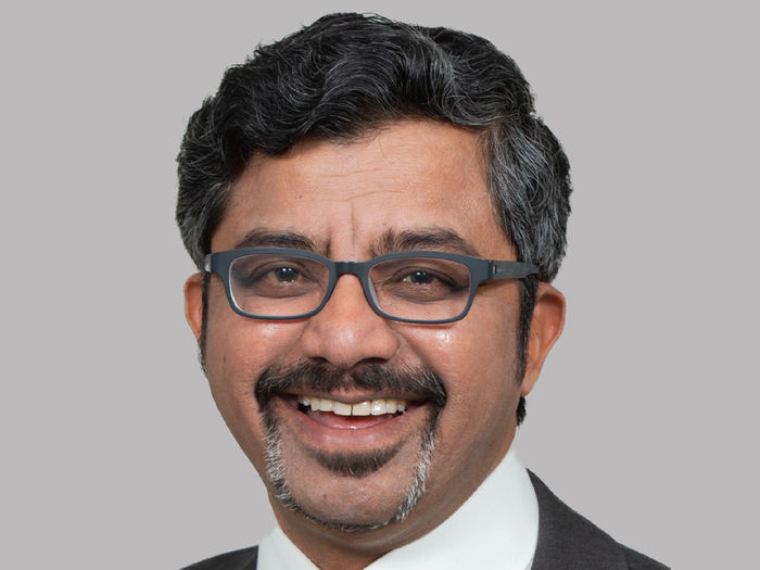 Male adult from India smiling with dark hair and wearing glasses