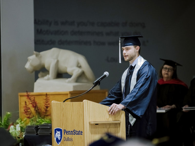 Male student in cap and gown giving a speech at commencement.