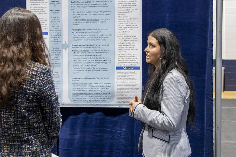 Young woman with long brown hair wears a gray blazer presenting research