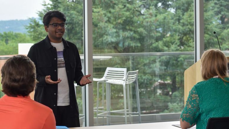 Young man standing in the front of a table presentaing to a male and female
