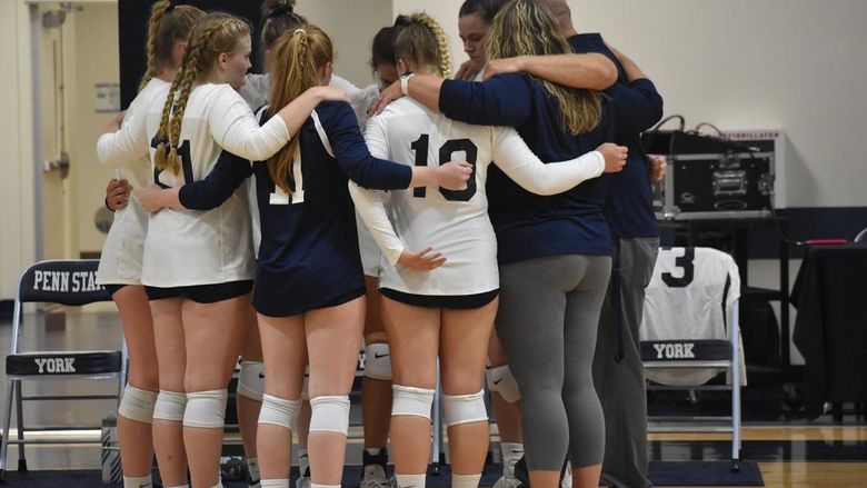 Women's volleyball players and coaches in a huddle on the basketball court