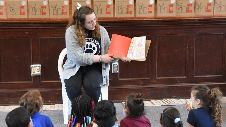 A Penn State York female student turns the pages of a book and reads to elementary school children.