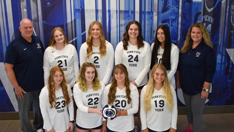 Eight femal volleyball players, dressed in uniform,  and a male and female coach.