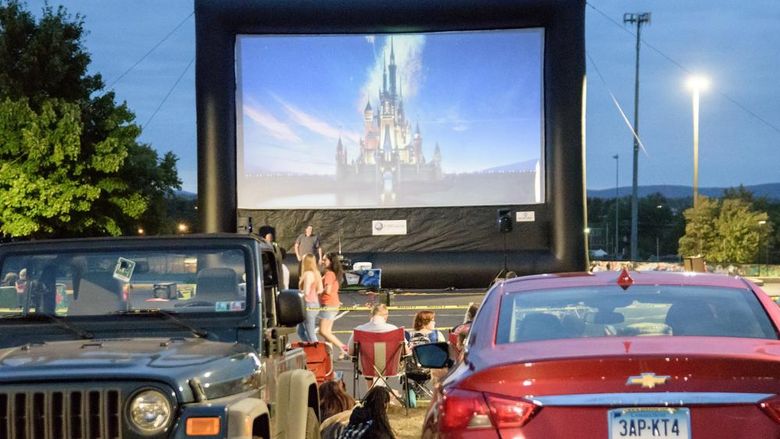 Inflatable rmovie screen with Disney insignia on it and cars parked in a lot in front of it.