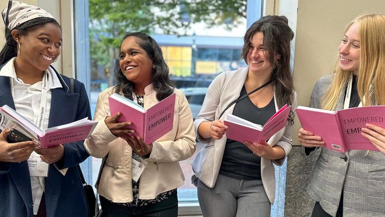 Four female students smile and hold pink journals they received as a gift from the Women's Philanthropic Network (WPN) at Penn State York