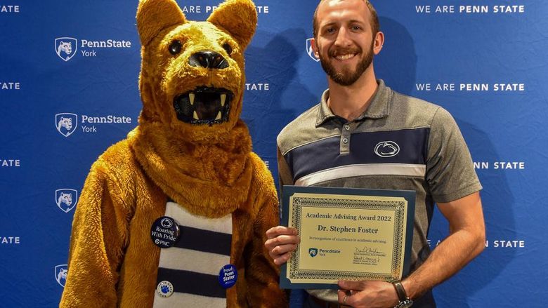 Penn State Nitttany Lion character shows off certificate with male faculty member who received it