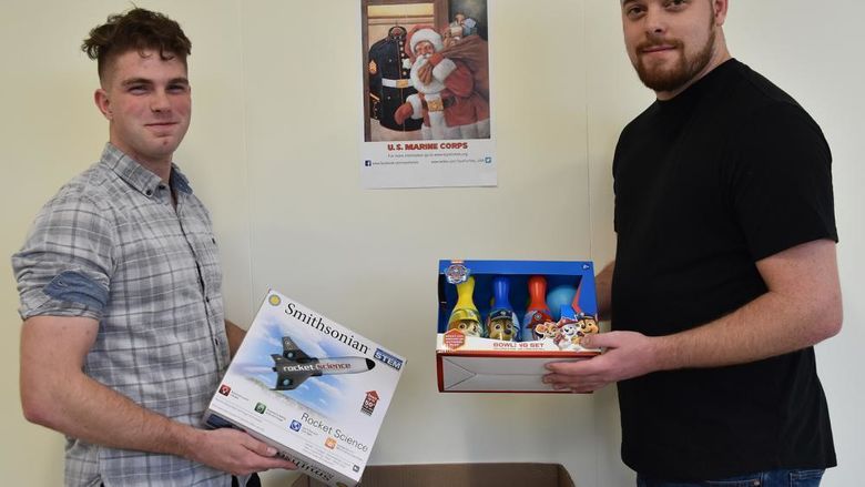 Toys for Tots  Collection box with male students each holding a toy to contribute