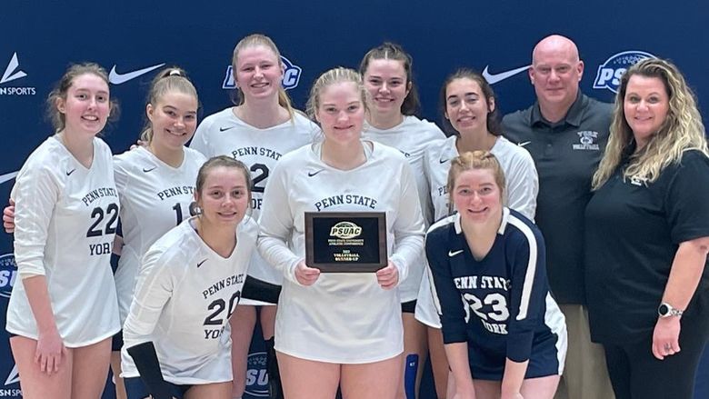 Eight female student-athletes iat Penn State York in volleyball uniforms and a female and male coach pose with award