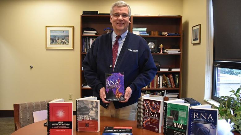 White older male wearing glasses with six books displayed on his desk.