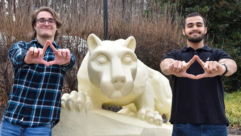 Two males flank the Nittany Lion Shrine at Penn State York and make a diamond shape with their fingers.