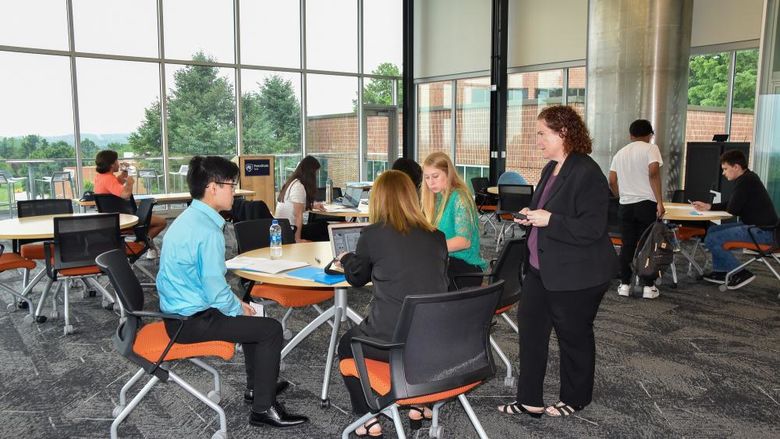 Faculty member  and groups of students arouind tables discussing work