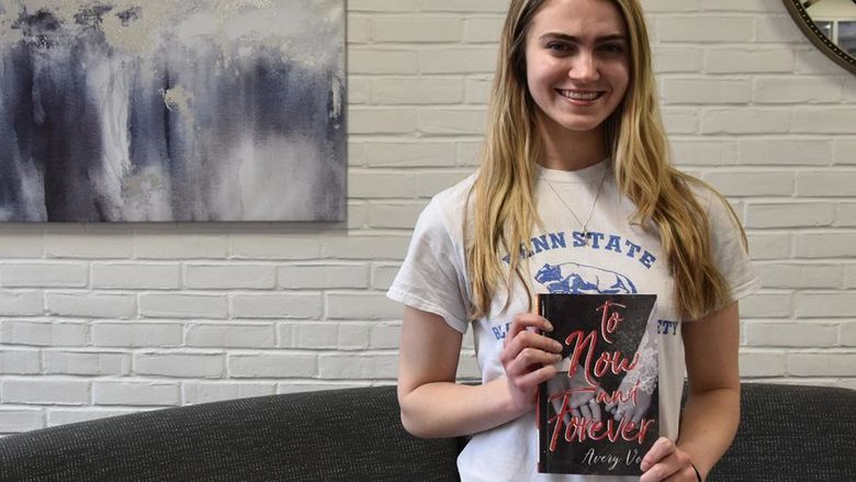 Young caucasian woman with long hair holding a book, art on the wall in the background.