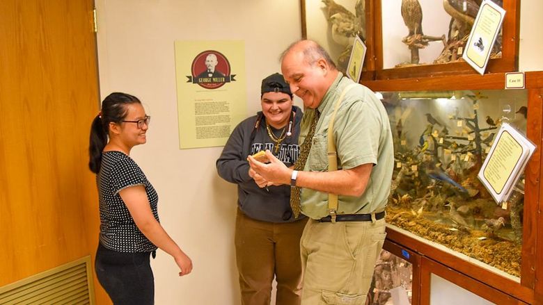 Two female students with a male faculty member examing a specimen at a museum