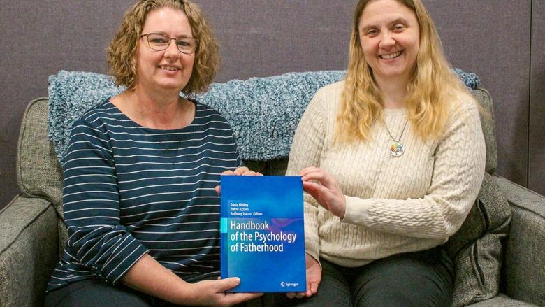 Two female faculty members sitting on a couch showing off their bool