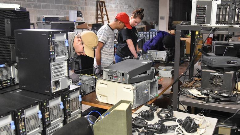 Group of students working  on computers and other electronics with pieces of equipment around the room